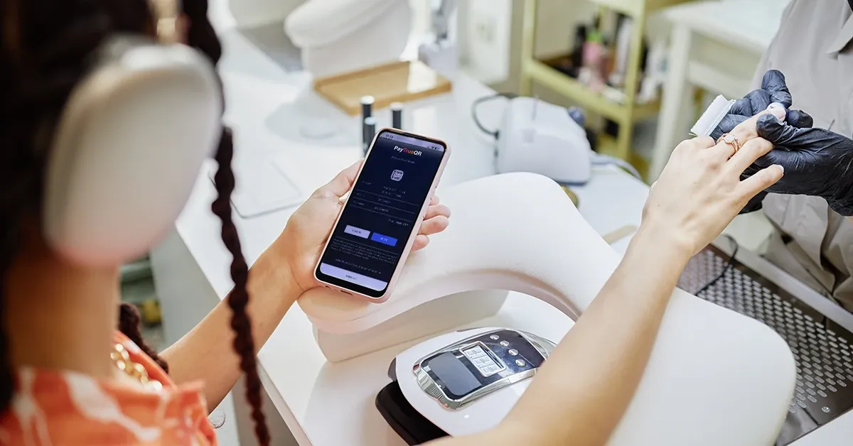 A customer at a nail salon holding a phone showing a PayTrueQR payment